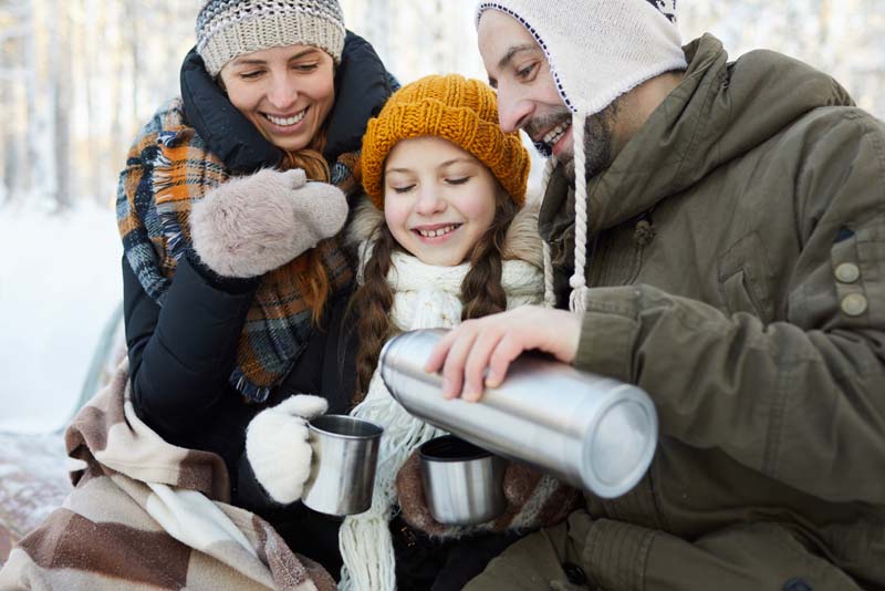 Image of a family sitting to enjoy a hot drink from a flask out in the snow.