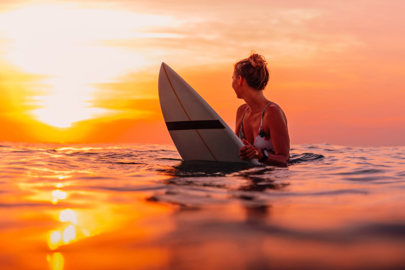 Image of a surfer sitting on a surfboard and watching the sunset.