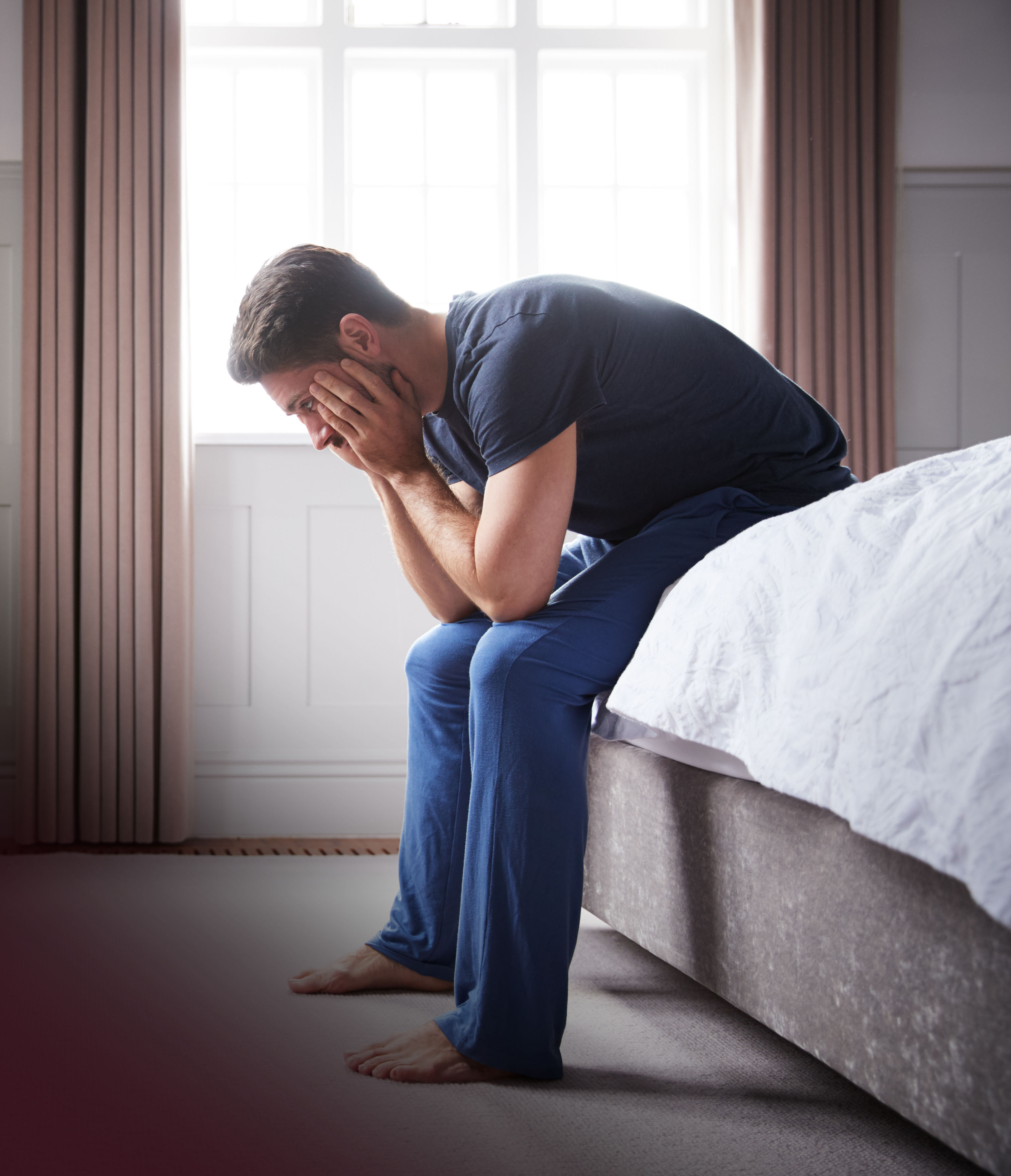 Man sitting on edge of bed with his head in his hands, looking worried.