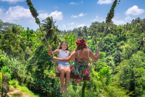 Travellers enjoying a rope swing above the trees in a tropical paradise.