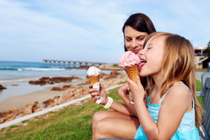 A mother and daughter enjoying ice creams by the seaside.