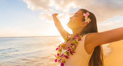 A woman wearing a lei on the beach at sunset.