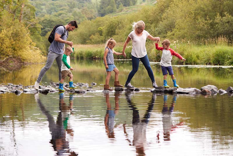 A young family trying to cross a shallow river in stepping stones.