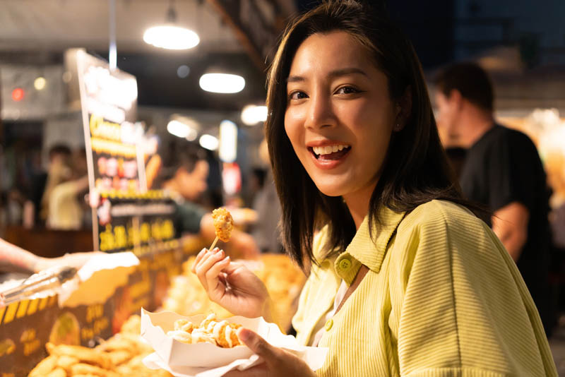 A young woman eating street food in a night market.