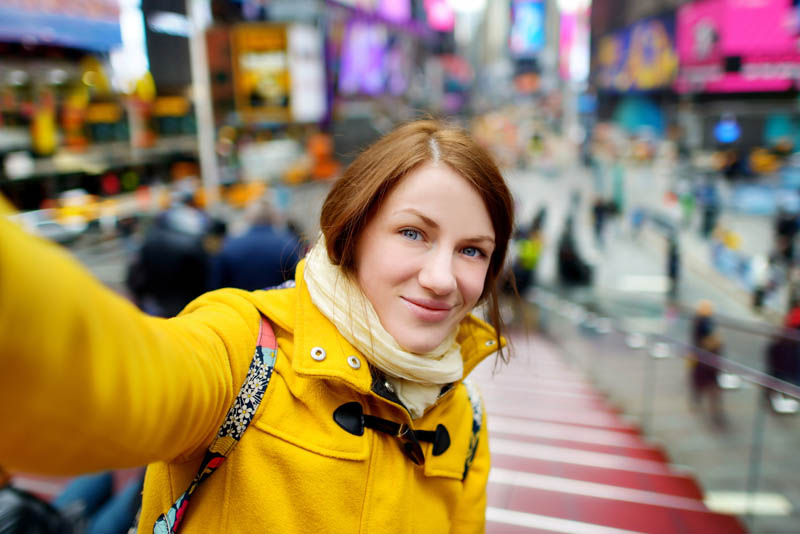 A woman taking a selfie, with a busy cityscape in the background.